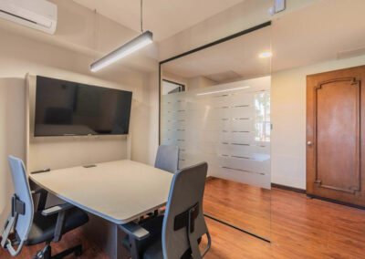 INterior de una sala de reuniones con mesa, tres sillas y un monitor led. División de vidrio esmerilado.
